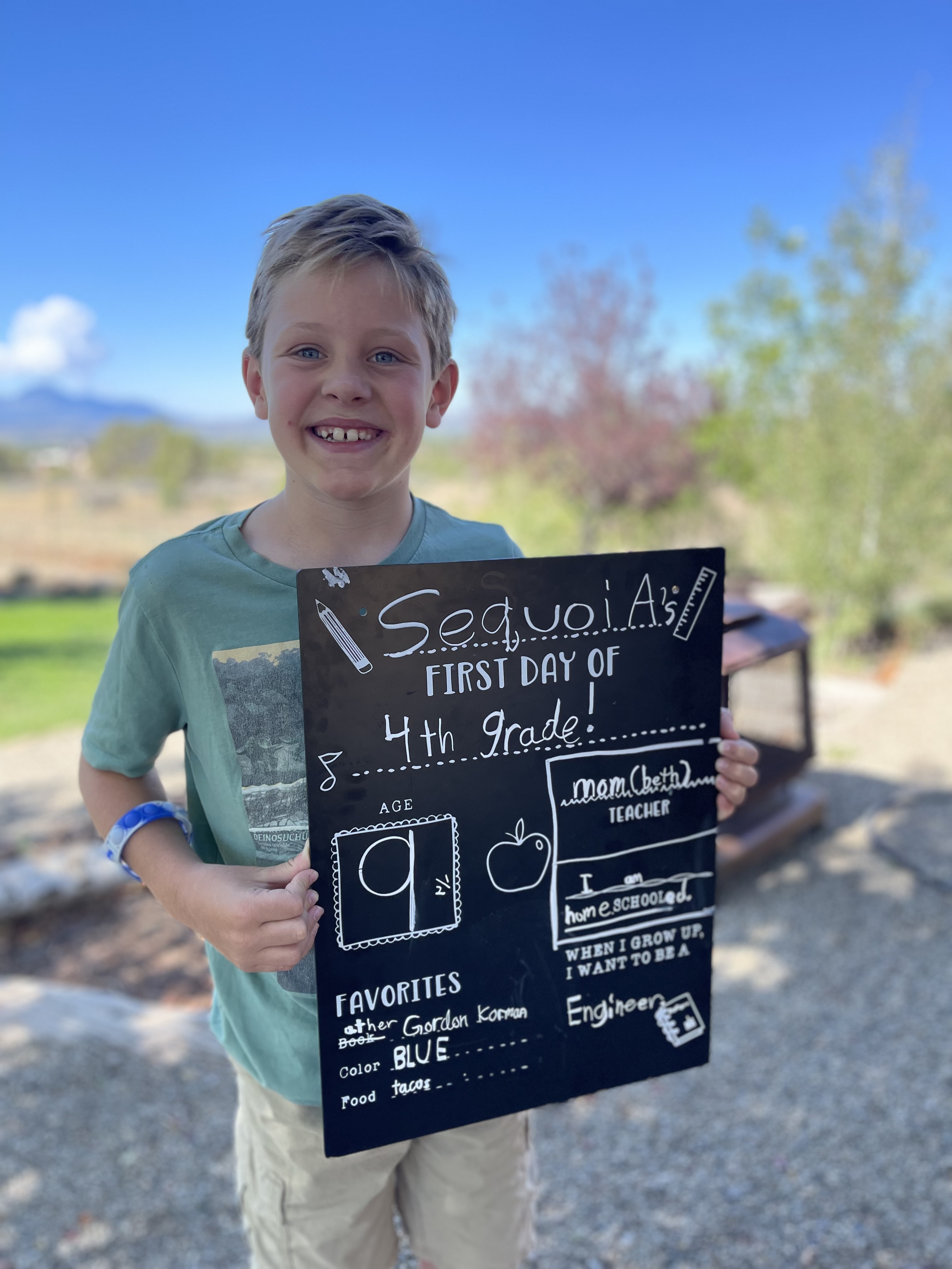 Bret James's son Sequoia smiling outdoors with his school sign